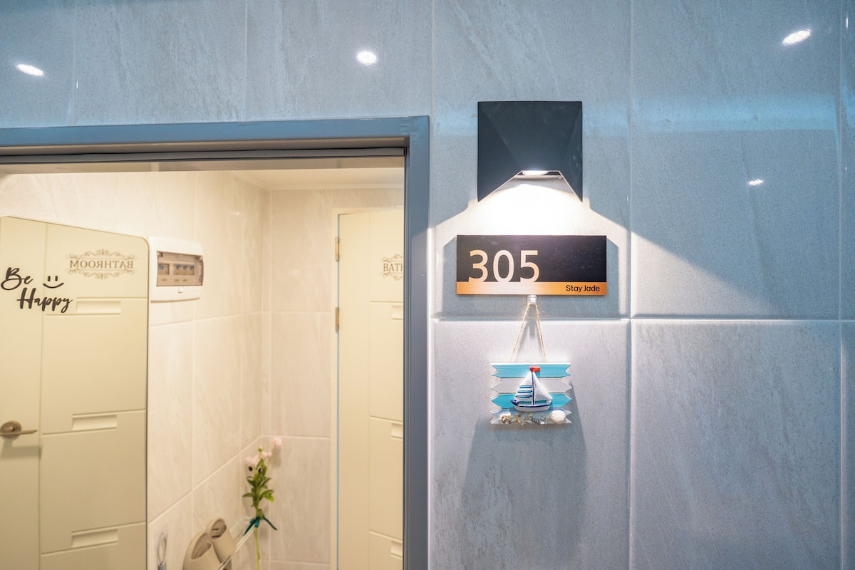 A bathroom with a white door, a towel rack, and a wall-mounted light fixture.