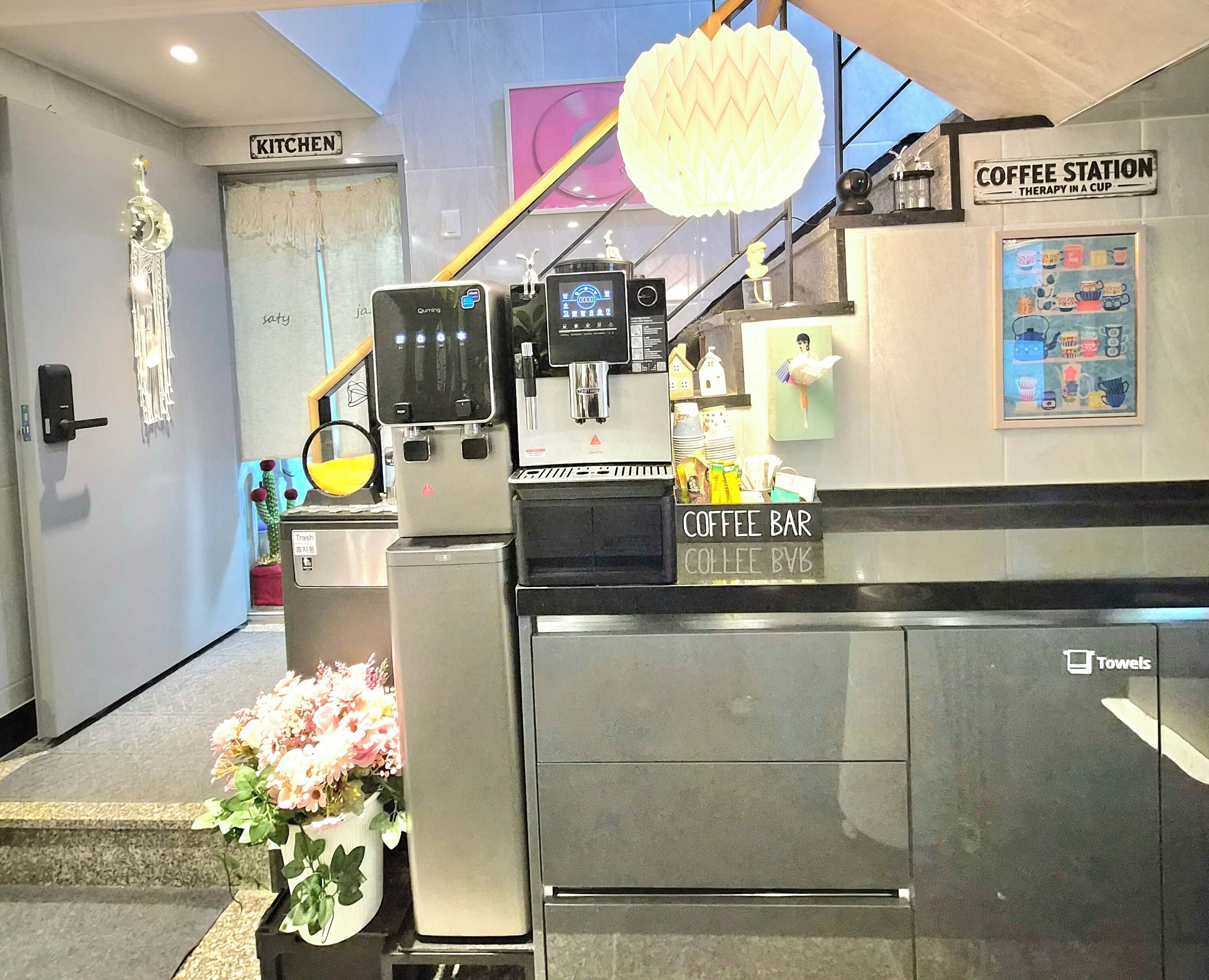 A coffee station with a sign, a trash bin, and a flower arrangement.