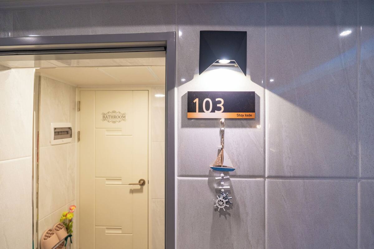 A bathroom with a sign reading '103 Stay Jade' and a small decorative sailboat.
