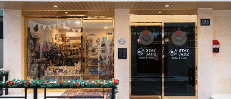 Exterior del Stay Jade, un Atelier & Hostel con entrada de vidrio, decoraciones navideñas y un banco afuera.