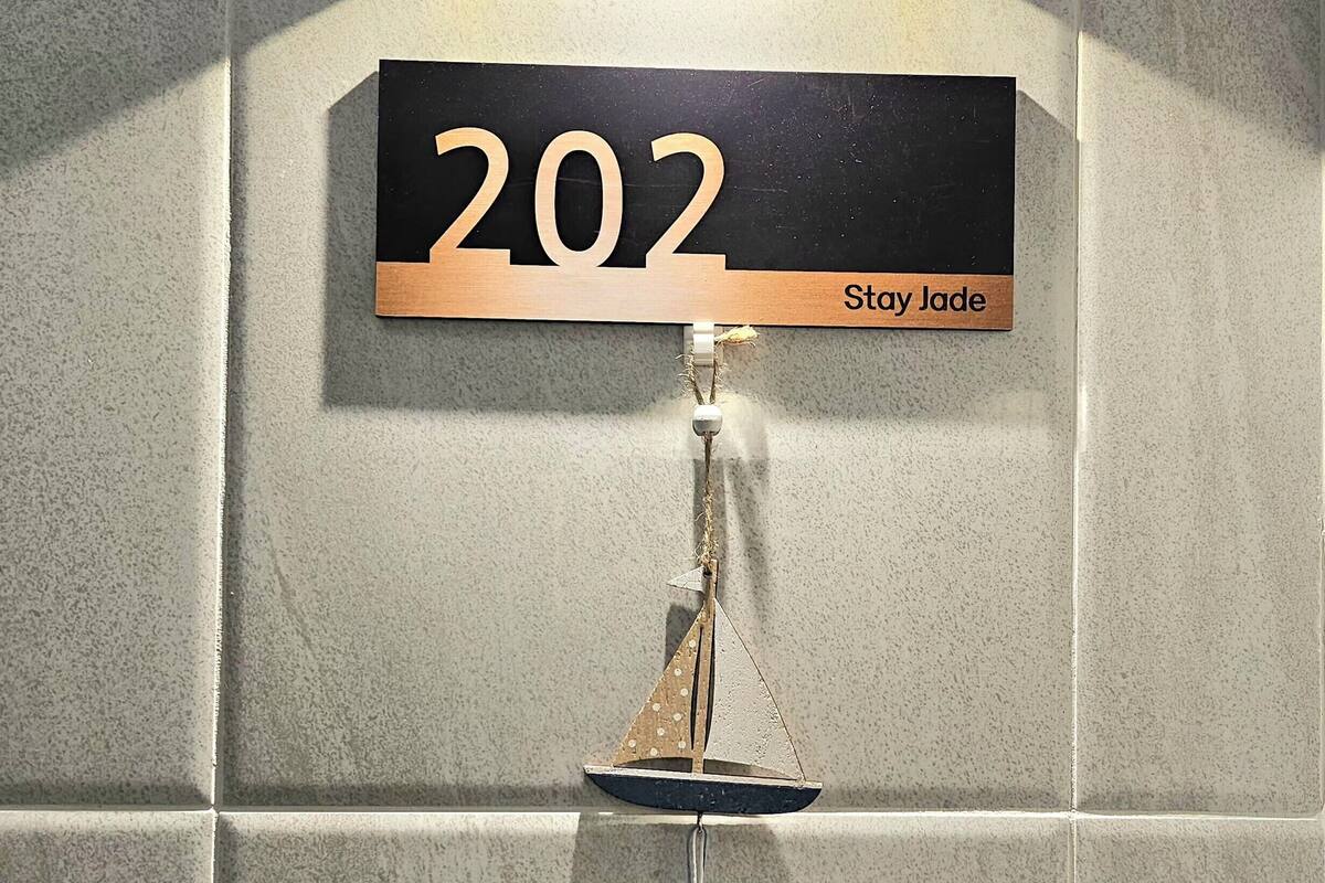 A room number sign '202' with a 'Stay Jade' label, a small sailboat decoration, and a light fixture above.