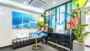 A reception area with a bench, a table with a blue tablecloth, a counter with stools, and a large window with a view of the sea. - STAY JADE (Seoul)