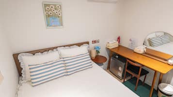 A neatly arranged hotel room with a bed, a desk, a chair, a small cabinet, and a trash bin.