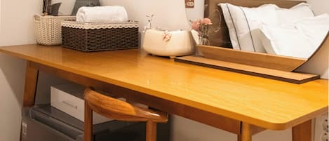 Une pièce de taille modeste, comprenant un bureau en bois, une chaise, un petit réfrigérateur, un miroir et une étagère fixée au mur, agrémentée d’un panier et d’un vase.