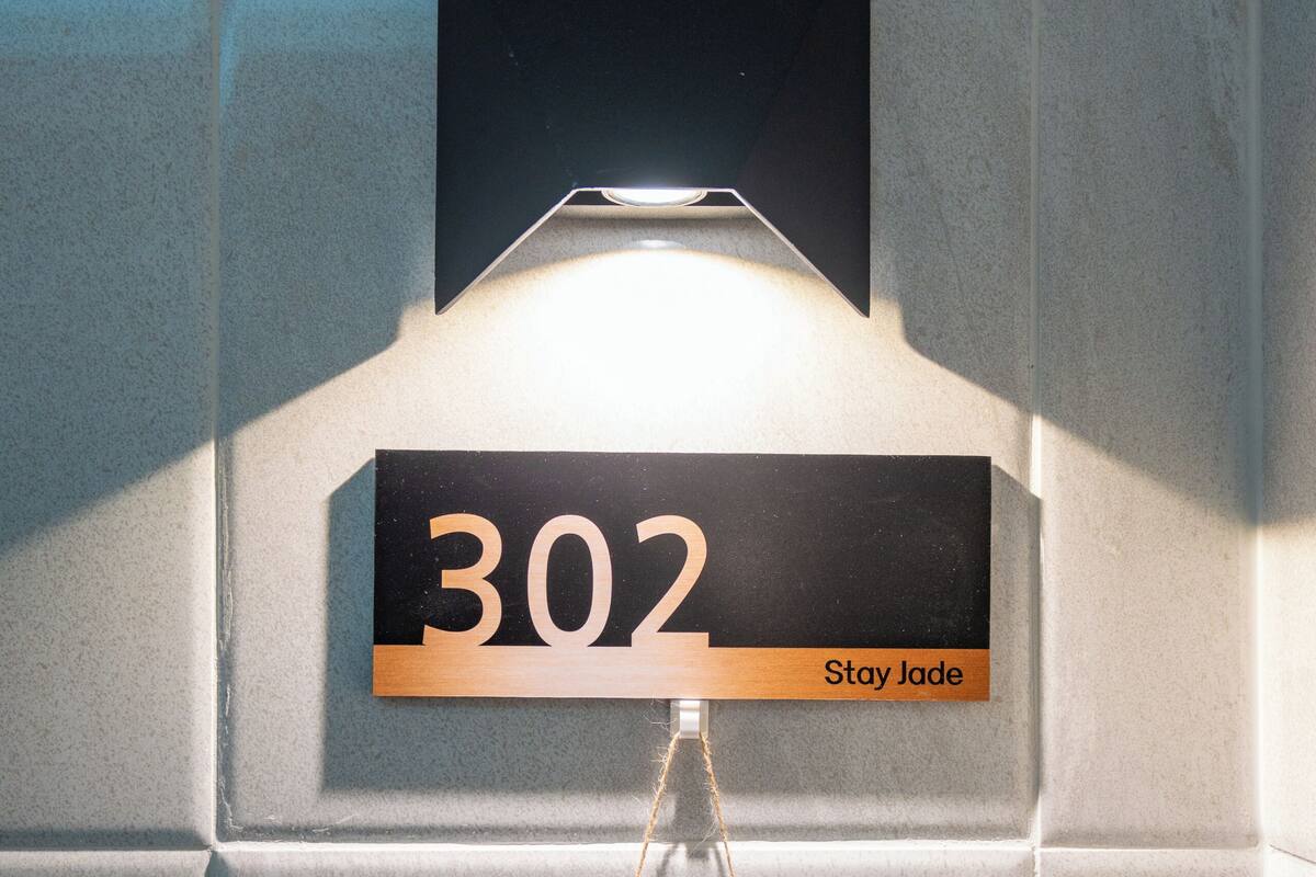 A wall-mounted sign with the number '302' and the text 'Stay Jade' on a tiled wall.