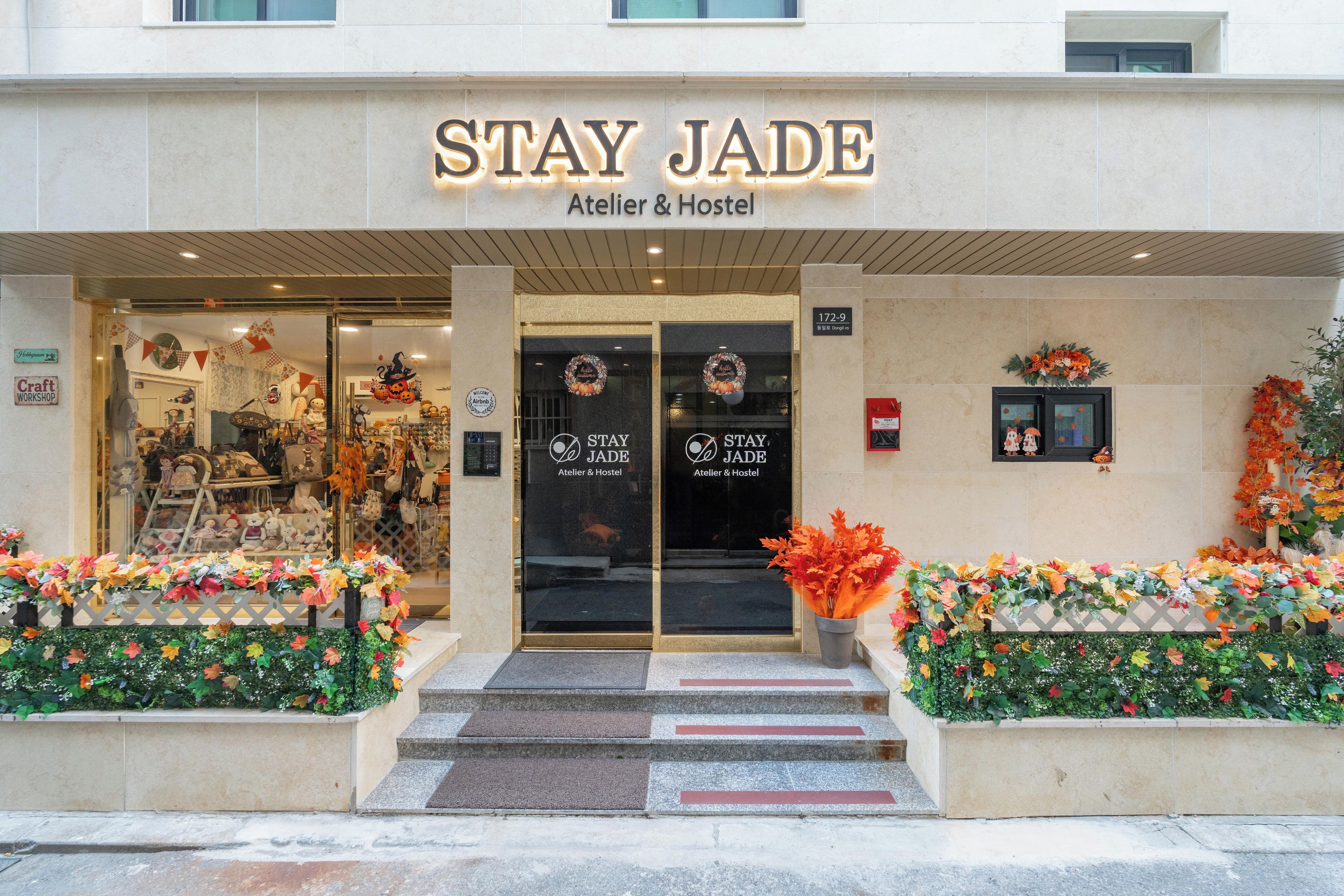 A storefront with a sign reading 'STAY JADE Atelier & Hostel' and a welcoming entrance with steps leading up to the door.