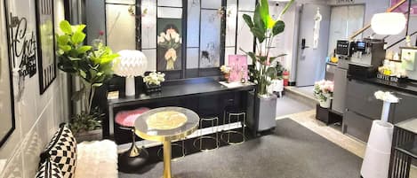 A modern hotel lobby with a reception desk, seating area, and a coffee bar.