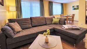 A modern living room with a sectional sofa, a dining table, and a vase with flowers on a coffee table. - Hotelpark Bodetal by Interhome (Thale)