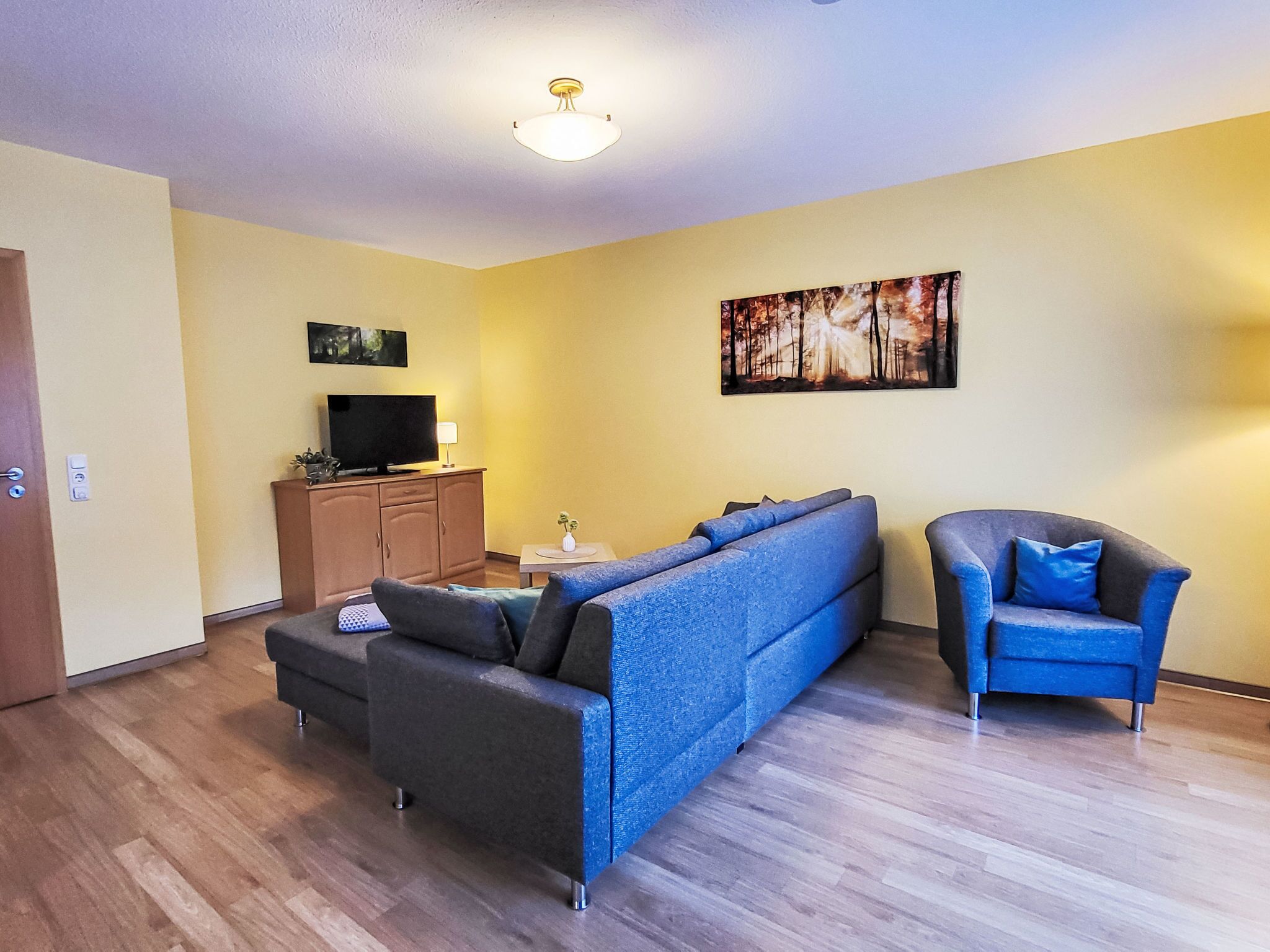 A living room with a sofa, a chair, a television on a cabinet, and a painting on the wall.