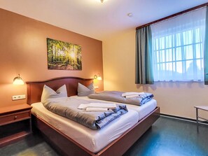 Une chambre d’hôtel avec un grand lit, deux tables de chevet, un tableau accroché au mur et une fenêtre avec des rideaux.