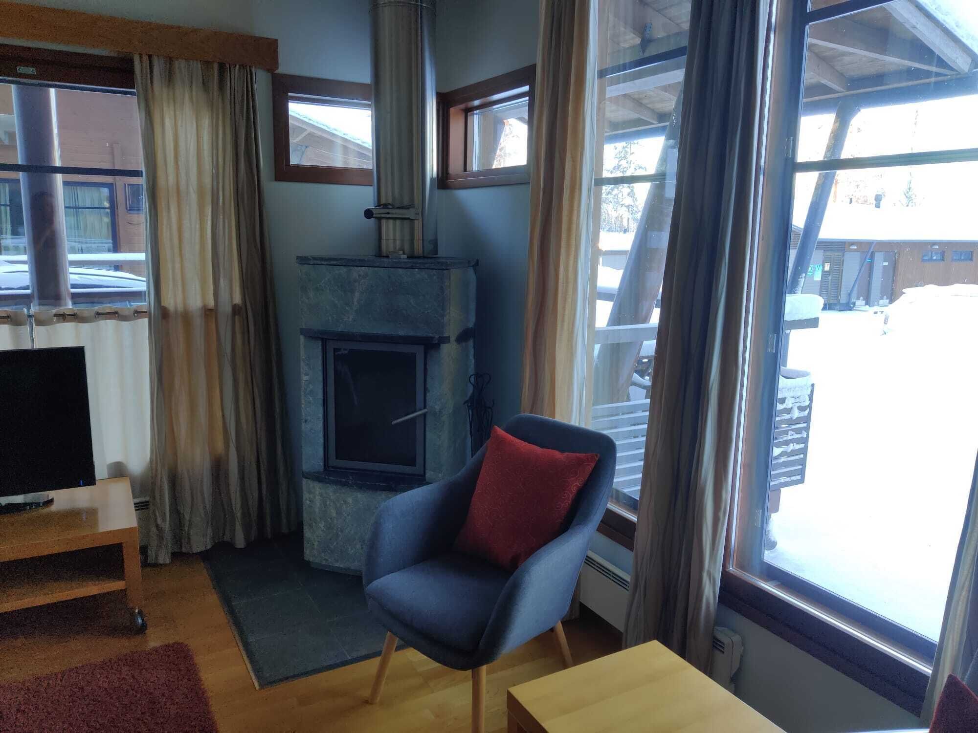 Una sala de estar acogedora con chimenea, un sillón cómodo, un televisor y ventanas amplias con vistas al exterior.