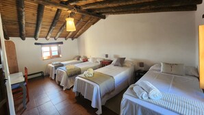 A rustic room with four beds, wooden beams on the ceiling, a small window, and a wooden chair. - CASA DE LA LUZ-FINCA LA SIERRA (Berzocana)