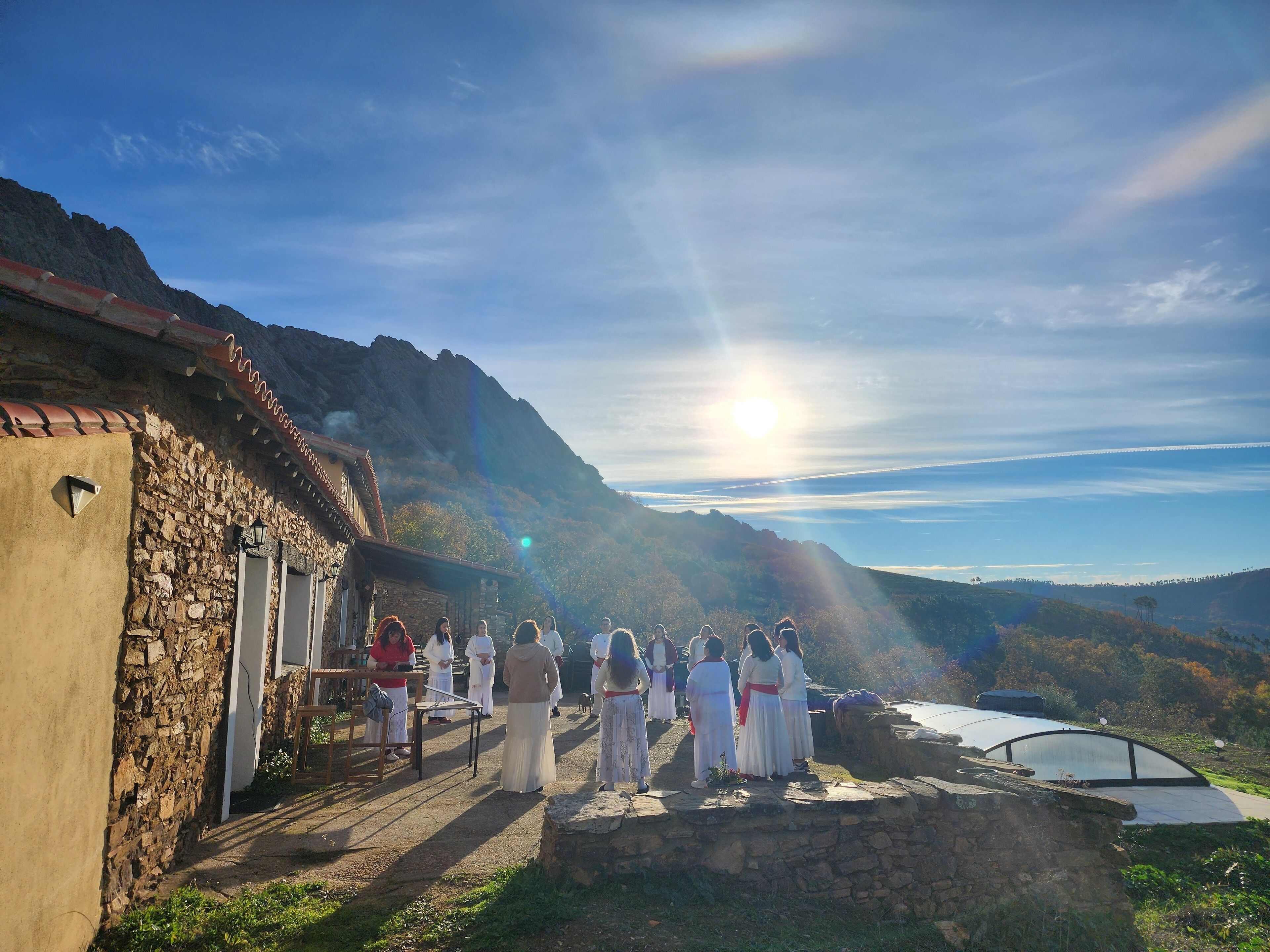 A group of people in traditional attire standing in front of a stone building with a mountainous backdrop.