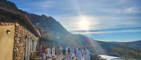 A group of people in traditional attire standing in front of a stone building with a mountainous backdrop.