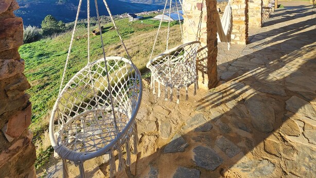 A rustic stone building with a wooden ceiling and a hanging chair. - CASA DE LA LUZ-FINCA LA SIERRA (Berzocana)
