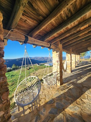 A rustic stone building with a wooden ceiling and a hanging chair. - CASA DE LA LUZ-FINCA LA SIERRA (Berzocana)