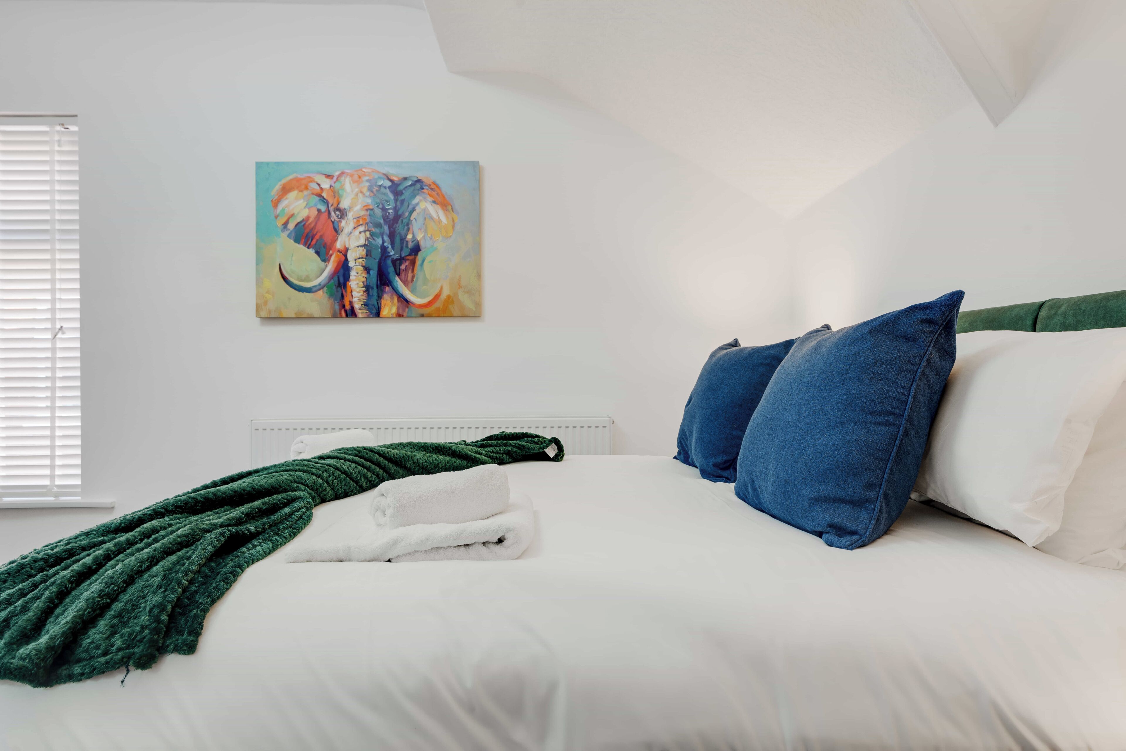 A bedroom with a bed, pillows, a blanket, and a painting on the wall.