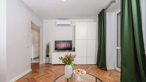 A modern living room with a flat-screen TV, a vase with flowers, and a plate of cookies on a glass table. - Lumina cozy apartment in the city center (Warsaw)