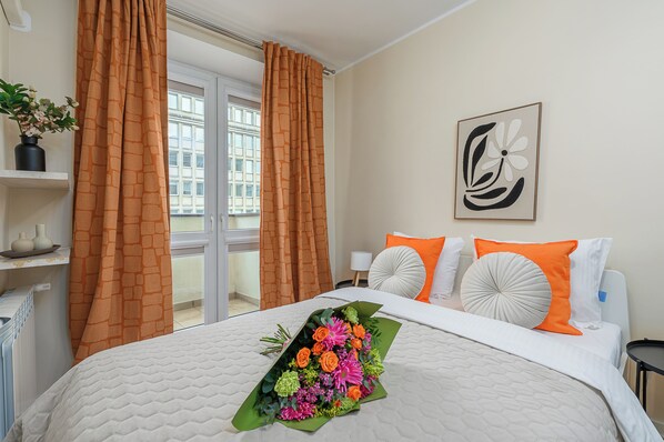 A hotel room with a bed, orange curtains, a window, a potted plant, and a painting on the wall. - Lumina cozy apartment in the city center (Warsaw)