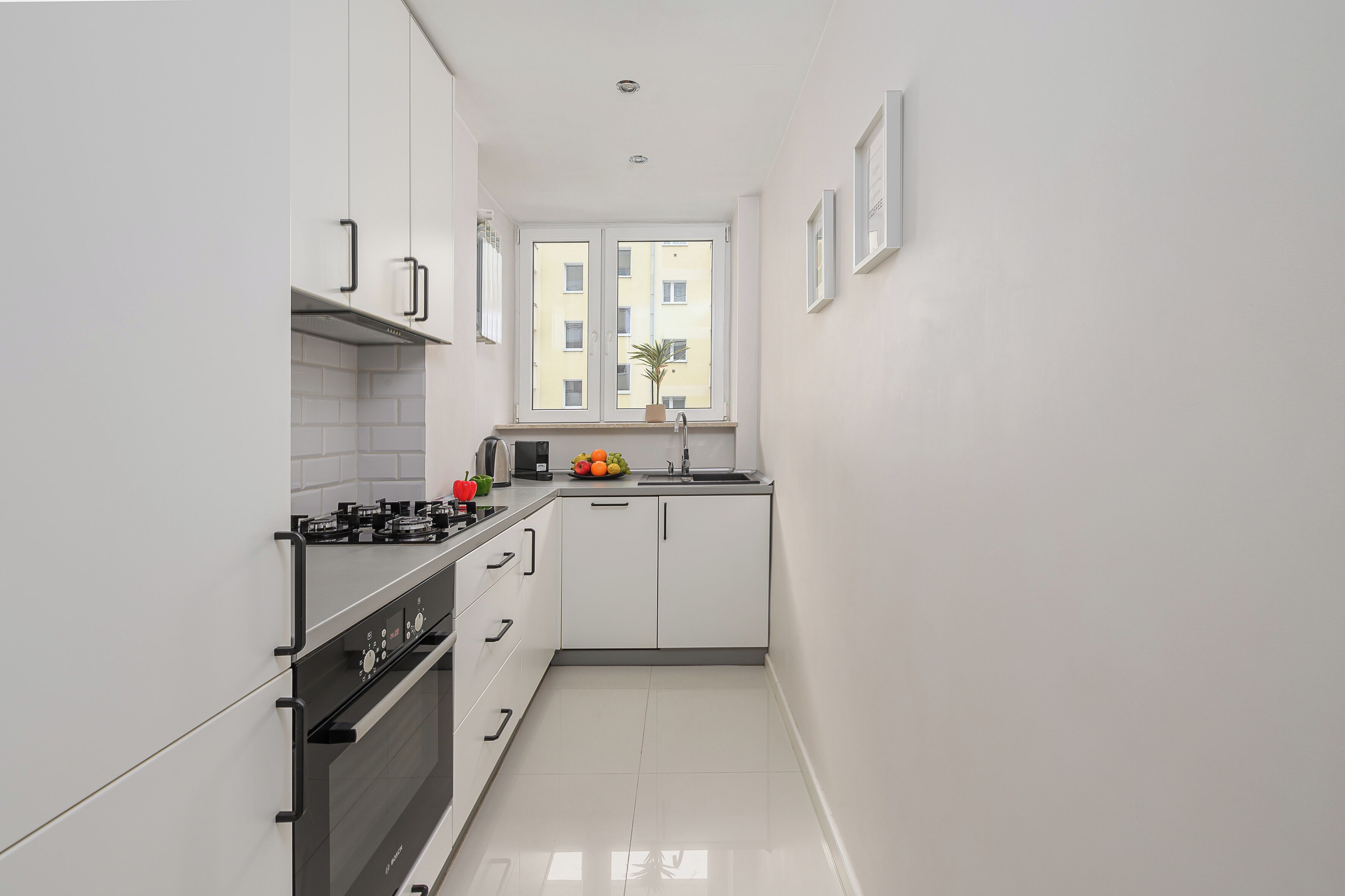 Cozinha pequena com armários brancos, fogão e janela com vista para edifícios.