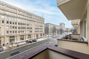 A view from a balcony overlooking a city street with a large building, a bus stop, and a pedestrian crossing. - Lumina cozy apartment in the city center (Warsaw)