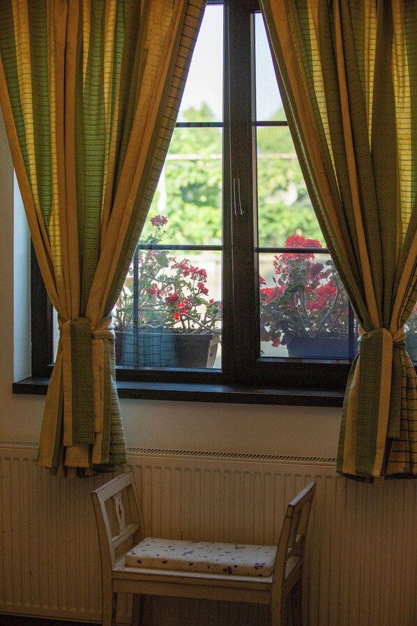 Una ventana con cortinas atadas, mostrando un balcón con plantas y flores en macetas.
