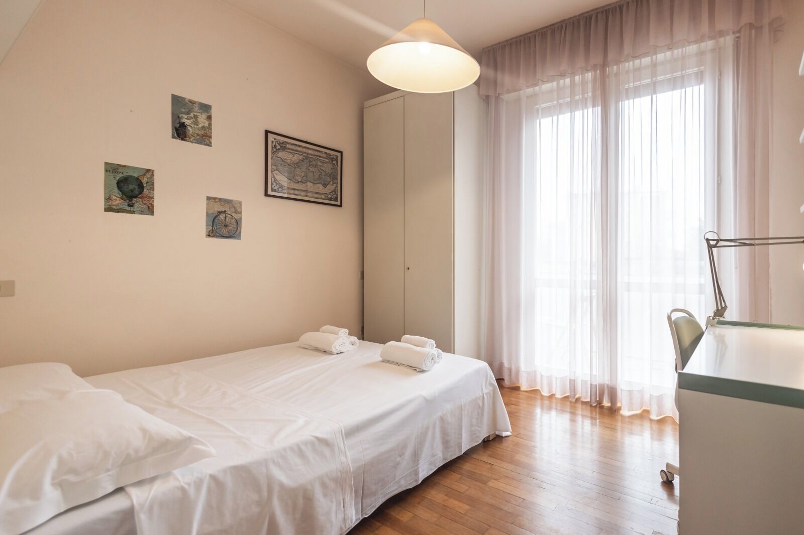 A bedroom with a single bed, a desk, and a chair. There are three framed pictures on the wall.