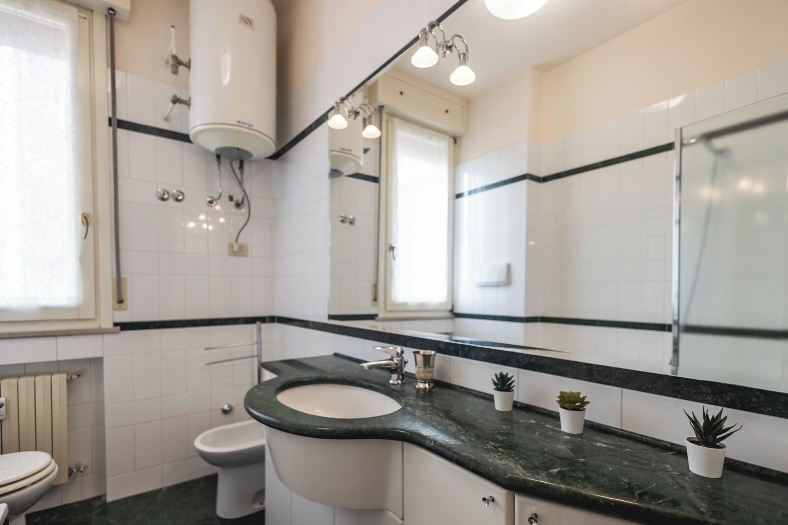 A modern bathroom with a white toilet, a sink with a black countertop, and a large mirror.