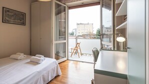 Une chambre à coucher comprenant un lit, une chaise, un bureau, une fenêtre et une vue sur les bâtiments environnants.