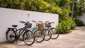 Three bicycles parked against a white wall with a concrete ground, surrounded by greenery. - Luna Studios 23  (Bacalar)