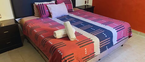 A bed with a patterned bedspread, pillows, and a rolled towel.