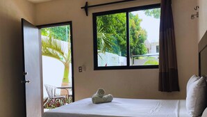 A hotel room with two beds, a ceiling fan, a window with curtains, and a view of greenery outside. - Luna Studios 23  (Bacalar)