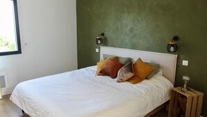 A bedroom with a large bed, green walls, two wall-mounted lamps, and a small wooden nightstand. - Pays Basque: Family home with large garden, close to mountains and ocean! (Mouguerre)