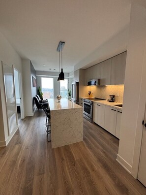 A modern kitchen with a central island, stainless steel appliances, and a view to the outside. - Elegant 2 Bedroom Suite in Toronto | Elm Ledbury (Toronto)