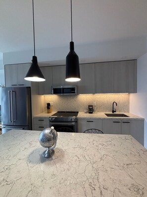 A modern kitchen with marble countertops, a stainless steel refrigerator, a built-in oven, and a coffee maker. - Elegant 2 Bedroom Suite in Toronto | Elm Ledbury (Toronto)