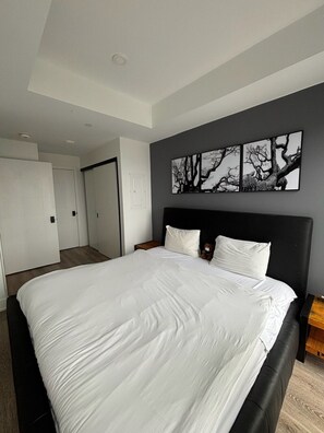 A modern bedroom with a large bed, a headboard, and a wall-mounted artwork. - Furnished 2 Bedroom with 2 Bathrooms in Toronto | Elm Ledbury (Toronto)