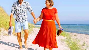 Una pareja caminando por un sendero arenoso junto a la playa, tomados de la mano.