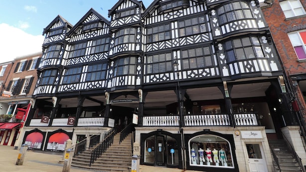 A traditional black and white timber-framed building with multiple floors, a central staircase, and a ground-level entrance with a shop on the right. - Central Vista Retreat (Chester)
