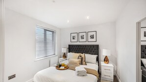 A bedroom with a large bed, two bedside tables, a window with blinds, and three framed pictures on the wall. - York Suite (Chester)