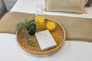 A breakfast tray with a book titled "Good Vibes, Good Life" by Vick King, a glass of orange juice, a glass of orange juice, and a potted plant on a bed with a beige blanket. - Grosvenor Apartment (Chester)
