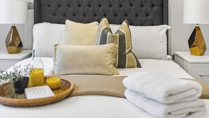 Ein ordentlich bezogenes Bett mit dunklem Kopfteil, mehreren Kissen und einem Nachttisch mit Lampe und Dekoration.