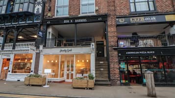A street view with a building housing 'EGO X BARBERS' and 'JAWNTY GOAT' on the ground floor, and 'AMERICAN PIZZA SLICES' on the second floor.