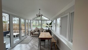 A sunroom with a herringbone floor, a wooden table, a sofa, and a chandelier. - Dolwen (Caernarfon)