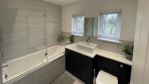 A modern bathroom with a bathtub, two sinks, and a shower. - Dolwen (Caernarfon)