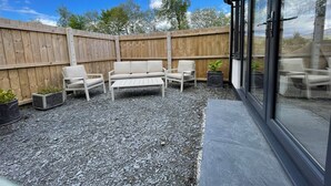 A patio with a wooden fence, a white sofa, two chairs, and a small table. - Dolwen (Caernarfon)