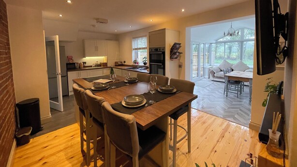 A modern kitchen with a dining area, wooden flooring, and a large window. - Dolwen (Caernarfon)