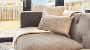 A grey sofa with a beige throw blanket and pillows in a room with large windows. - Newland Suite (Chester)
