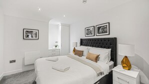Ein modernes Schlafzimmer mit einem großen Bett, Nachttischen, einem Spiegel und gerahmten Bildern an der Wand.