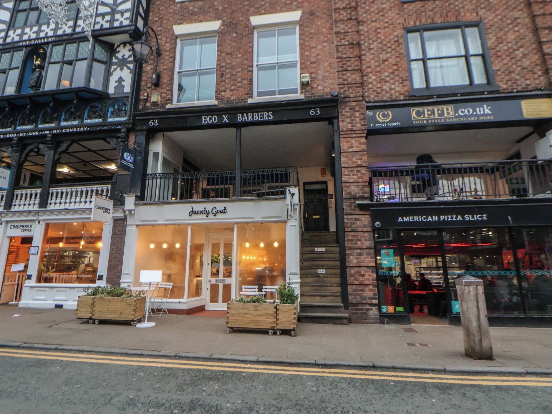 A street view with a building housing 'EGO X BARBERS' and 'JAWNTY GOAT' on the ground floor, and 'AMERICAN PIZZA SLICES' on the second floor.