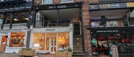 A street view with a building housing 'EGO X BARBERS' and 'JAWNTY GOAT' on the ground floor, and 'AMERICAN PIZZA SLICES' on the second floor.